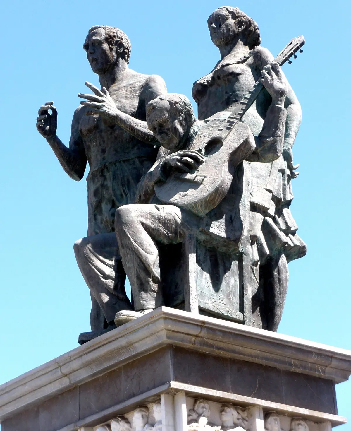 The bronze Monument to Flamenco in Granada, showing a seated guitarist, a singer and a dancer on a stone plinth against a blue sky